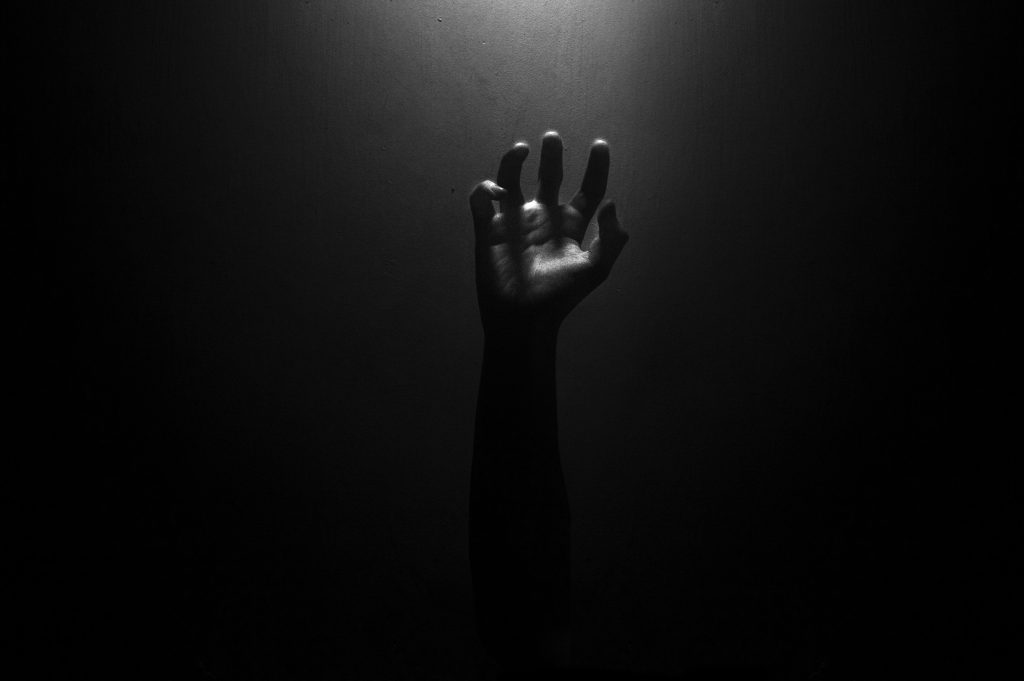 A solitary hand reaching upward contrasted against a dark backdrop, creating an eerie effect.